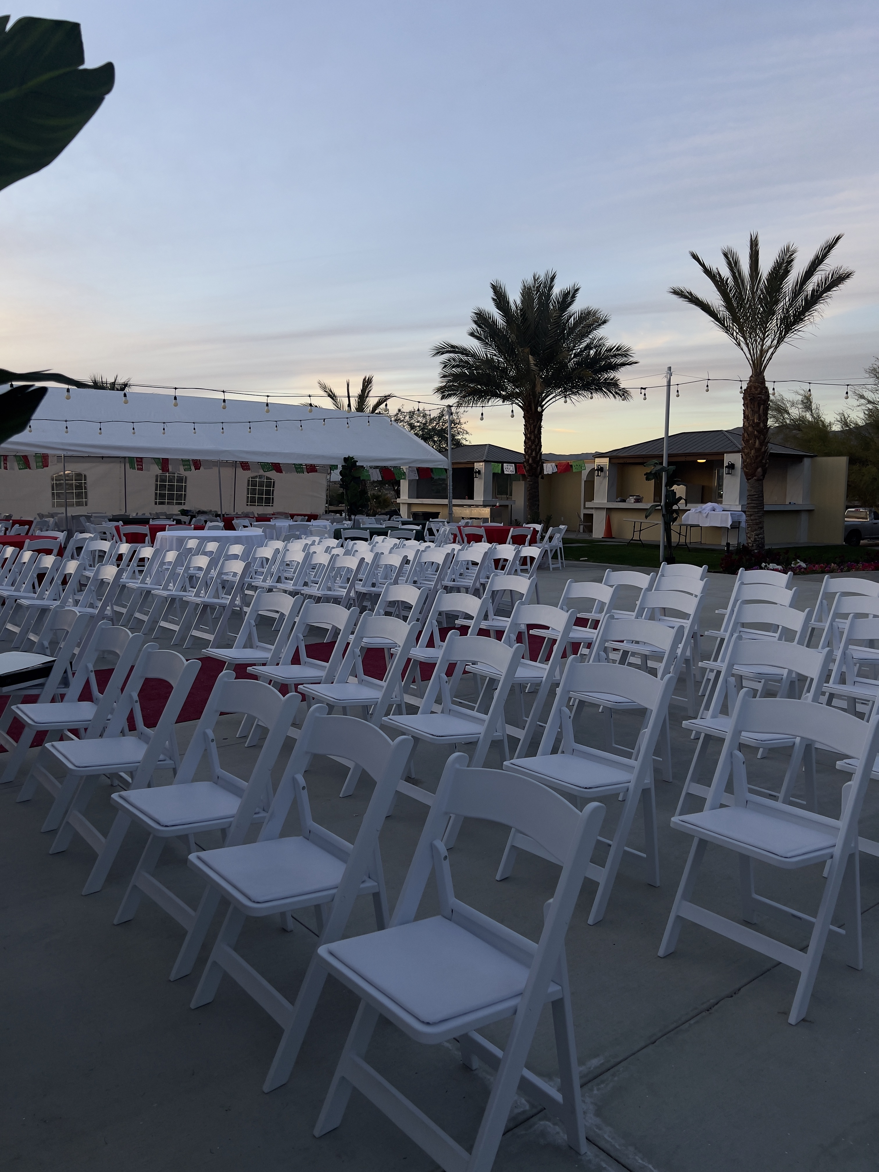 Rows of white resin folding chairs set for a ceremony under a canopy